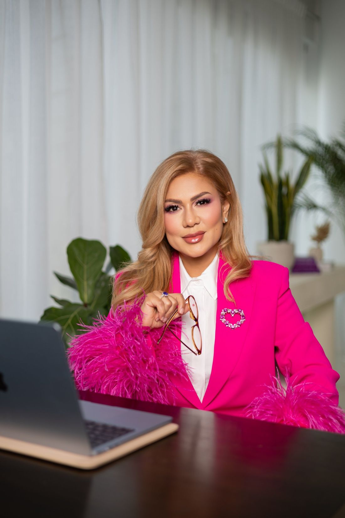 Wardah Harharah in a pink jacket at her desk, holding her glasses